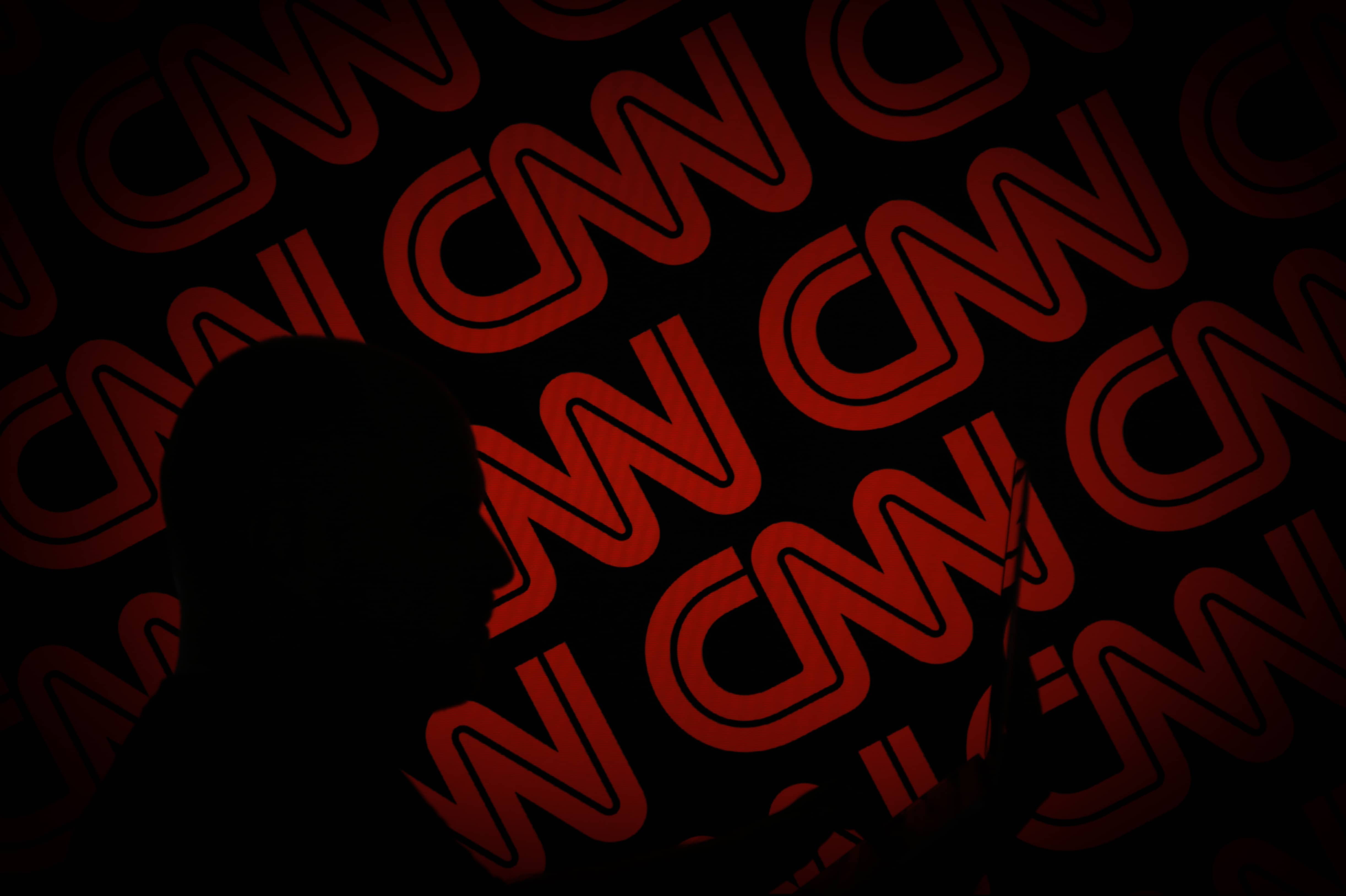 A man is seen holding with a smart device in front of a CNN logo in this photo illustration on 2 July, 2017.