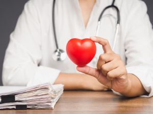 Doctor holding a red heart shape symbol while sitting in the hospital.