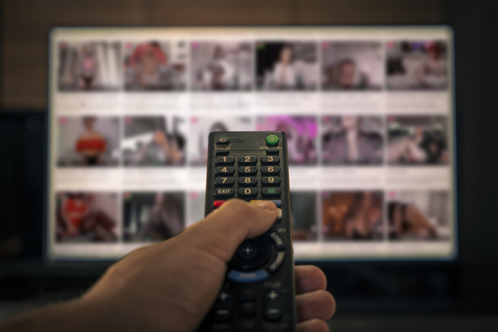 Porn TV pornography. remote control in a man's hand on the background of an erotic movie in out of focus. adult content on the cable channel in the hotel