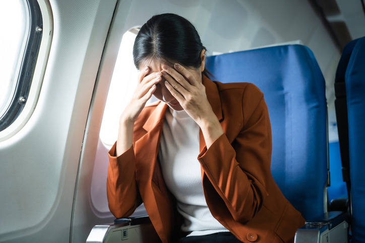 A young Asian woman, an airplane passenger, sits by the window seat, experiencing nausea and dizziness during the flight, which adds to her travel discomfort.