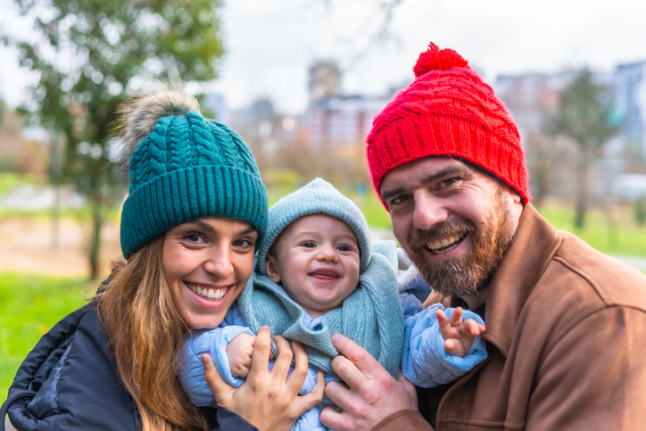 Happy family smiling and holding baby in park during winter