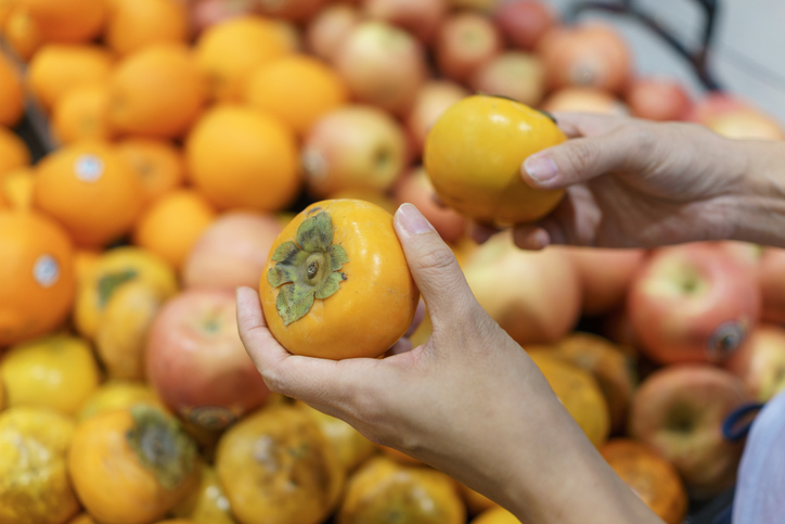 Customer Selecting Persimmons in a Supermarket