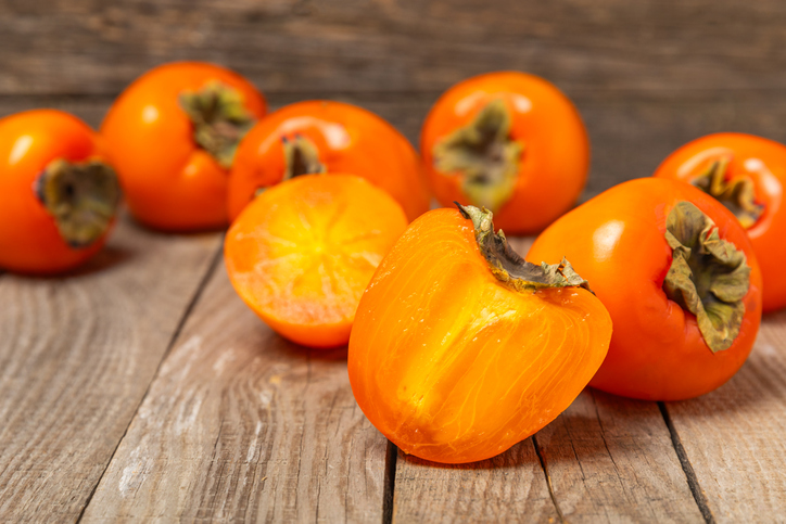 Persimmon on textured wooden background. Persimmon fruit. A piece of ripe, juicy, sweet persimmon fruit. Vegan. Orchard. Close-up. Space for text. Copy space.