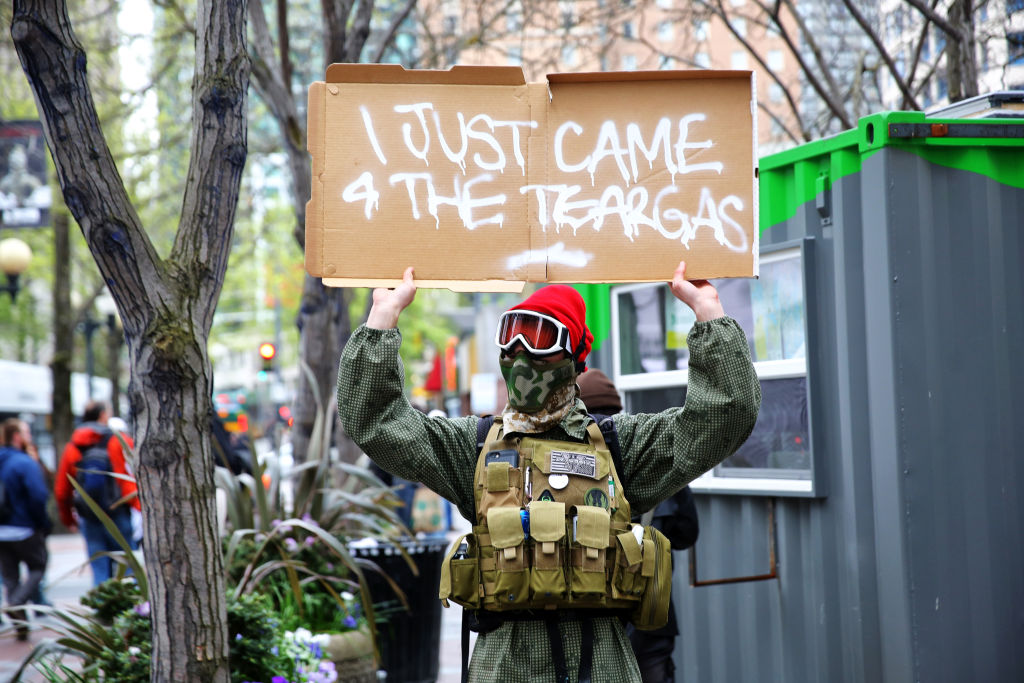 A man in a mask and goggles holds a sign reading ""I just came 4 the tear gas"" as anti-fascist demonstrators clash with Trump supporters and police at Westlake Park during an evening demonstration, May Day 2017 in Seattle. (Genna Martin, seattlepi.com)