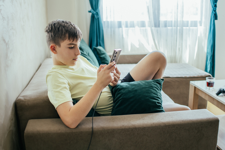 Everyday Electricity. Young boy playing video games on his mobile phone at home while phone is charging.