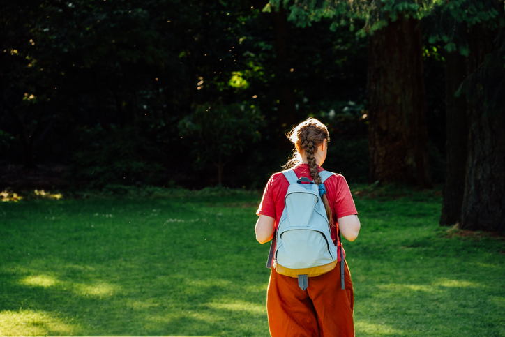 Lady with backpack walking through a sunny park in the afternoon