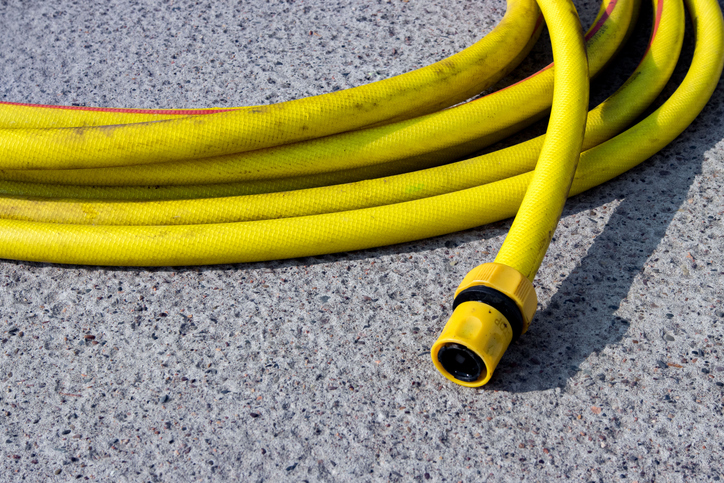 Bright yellow garden hose coiled neatly on a rough stone surface in a sunny outdoor setting