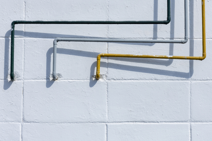 Asymmetrical yellow, gray and green pipes on a white brick wall