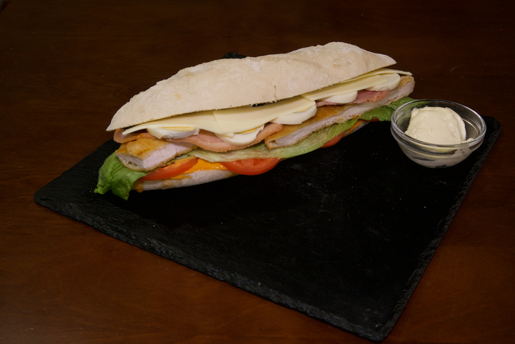 A sandwich with ham, lettuce, and tomato sits on a black table