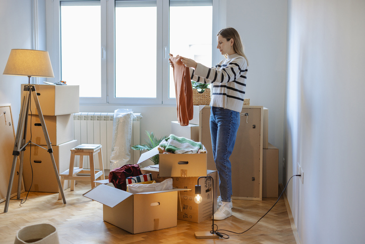 Young woman organizing clothes in a box among moving boxes in a bright room
