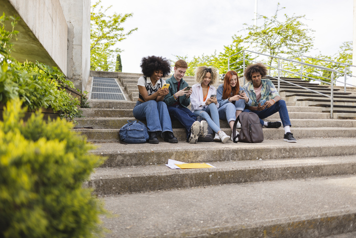 Group of university student friends sitting together using mobile phones to share content on social media